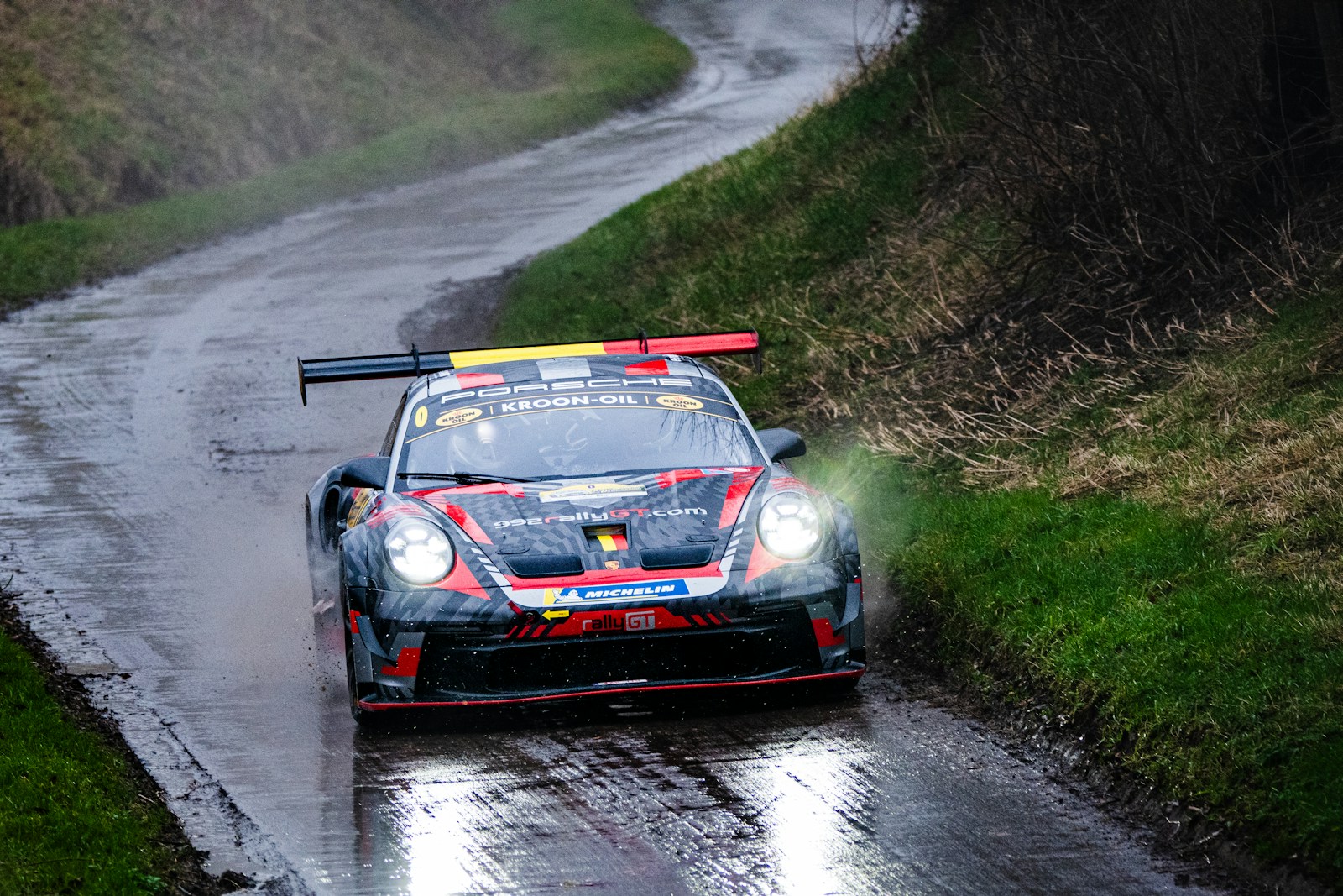 Photo by Xavier Praillet A car driving down a wet road in the rain